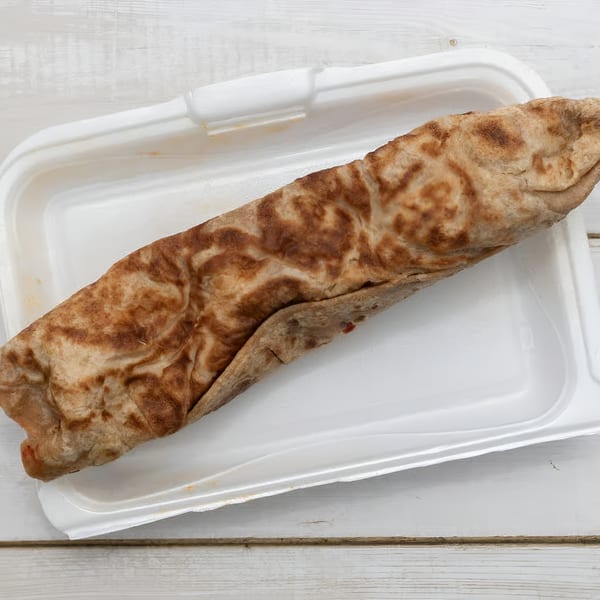 A large, golden-brown African Paradise Restaurant wrap rests in a white takeout container on a wooden table.