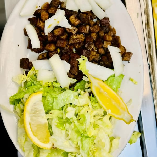 African Paradise Restaurant's dish with diced meat, onions, lettuce, and lemon wedges on a white plate.