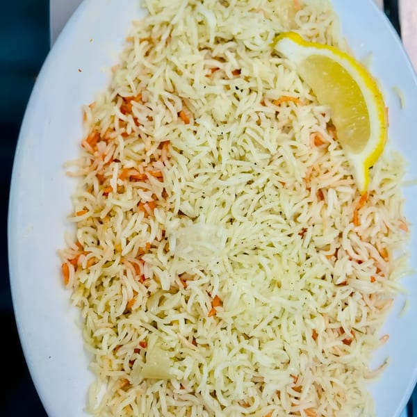 A white plate filled with African-style rice, featuring white and orange grains, garnished with a lemon wedge.
