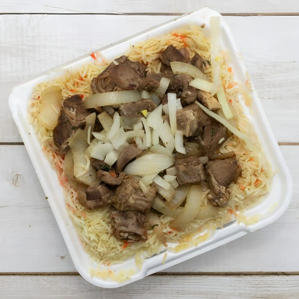 African Paradise Restaurant's rice dish with chunks of meat and sliced onions in a white takeout container.