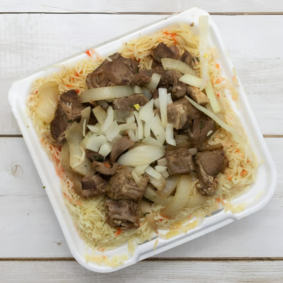 African Paradise Restaurant's rice dish with chunks of meat and sliced onions in a white takeout container.