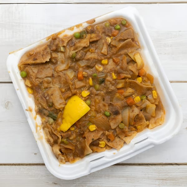 African stew with flatbread, corn, peas, and carrots in a white takeout container.